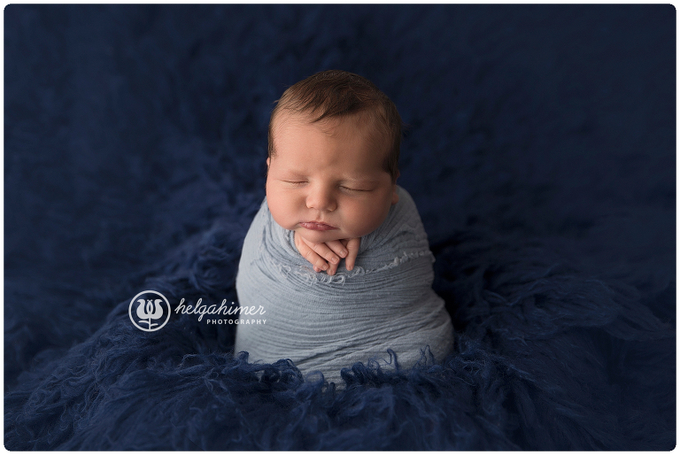 potato sack pose newborn baby wrapped in blue cheesecloth and on a dark blue flokati photographed in studio