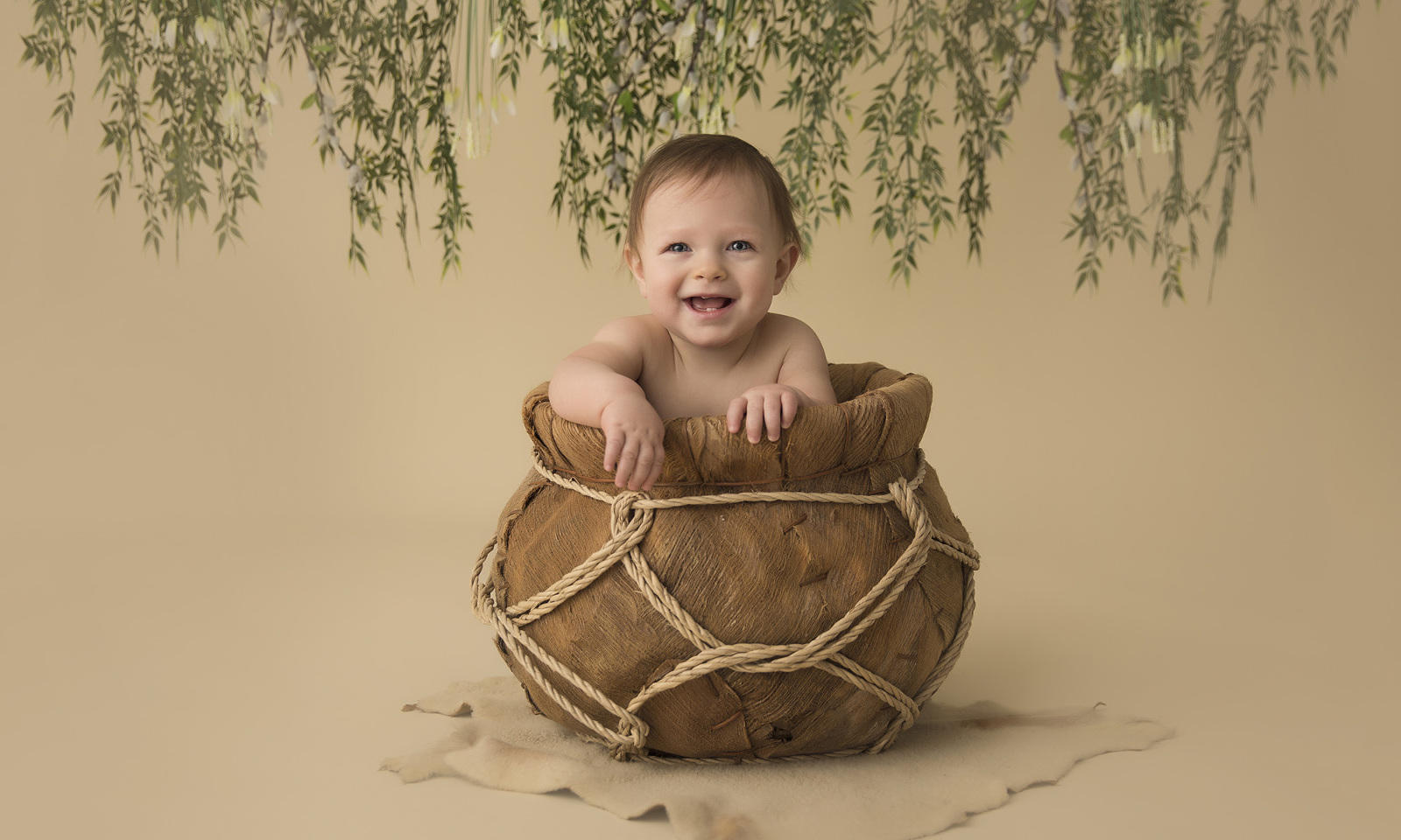 Studio child portrait session, the six-month-old child smiles and faces forward, sitting in a brown gourd container. Image by Helga Himer Photography, Sudbury, Ontario.